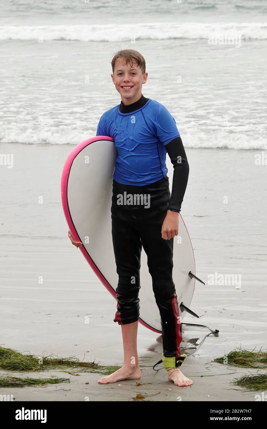 A 12 year old boy holds a surfboard after riding some waves. Stock Photo