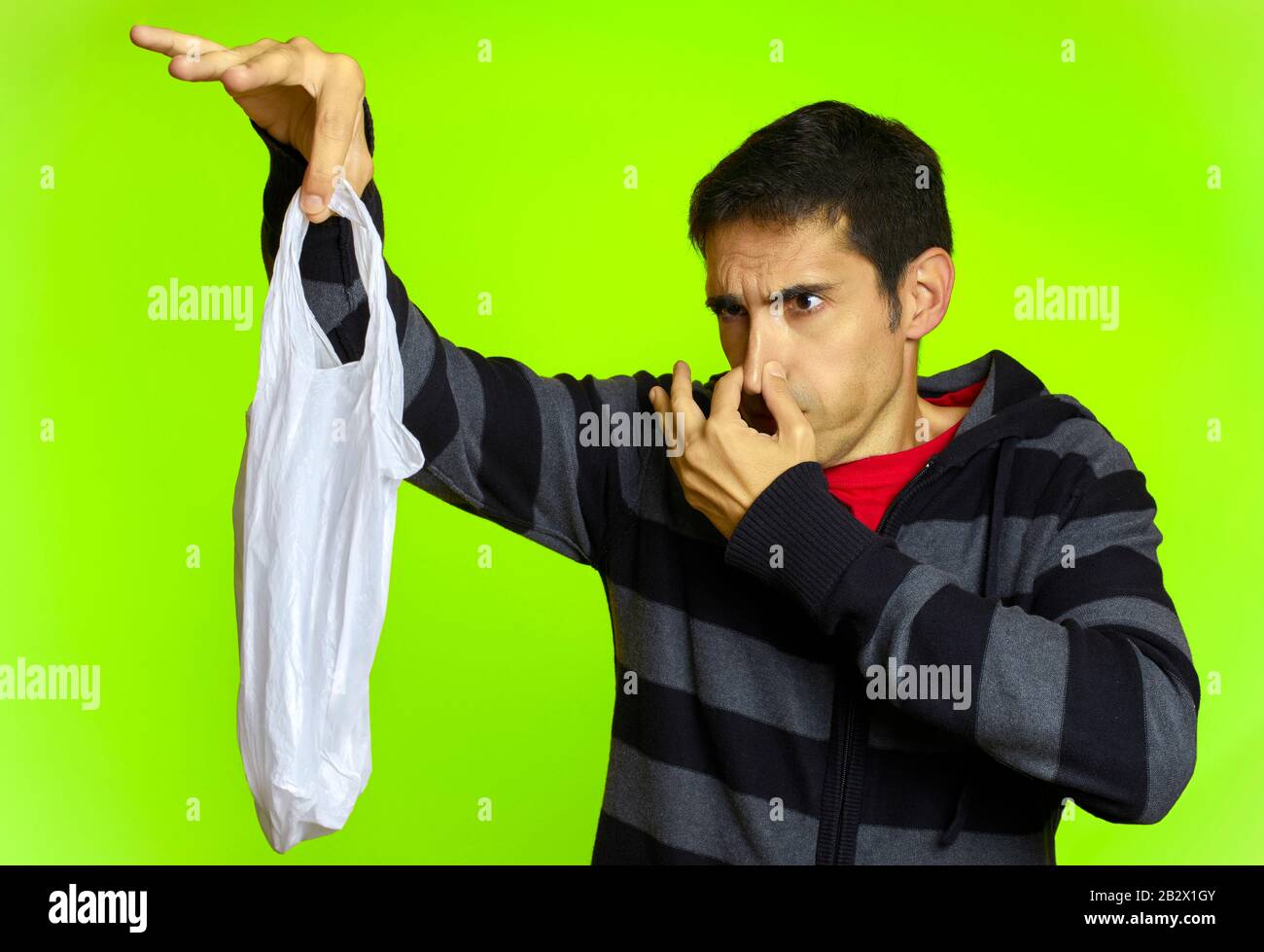 A man covering his nose with disgust holds a plastic bag in front of a green background Stock Photo