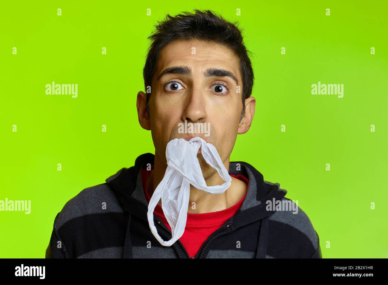 A choked man with a plastic bag in his mouth in front of a green background Stock Photo
