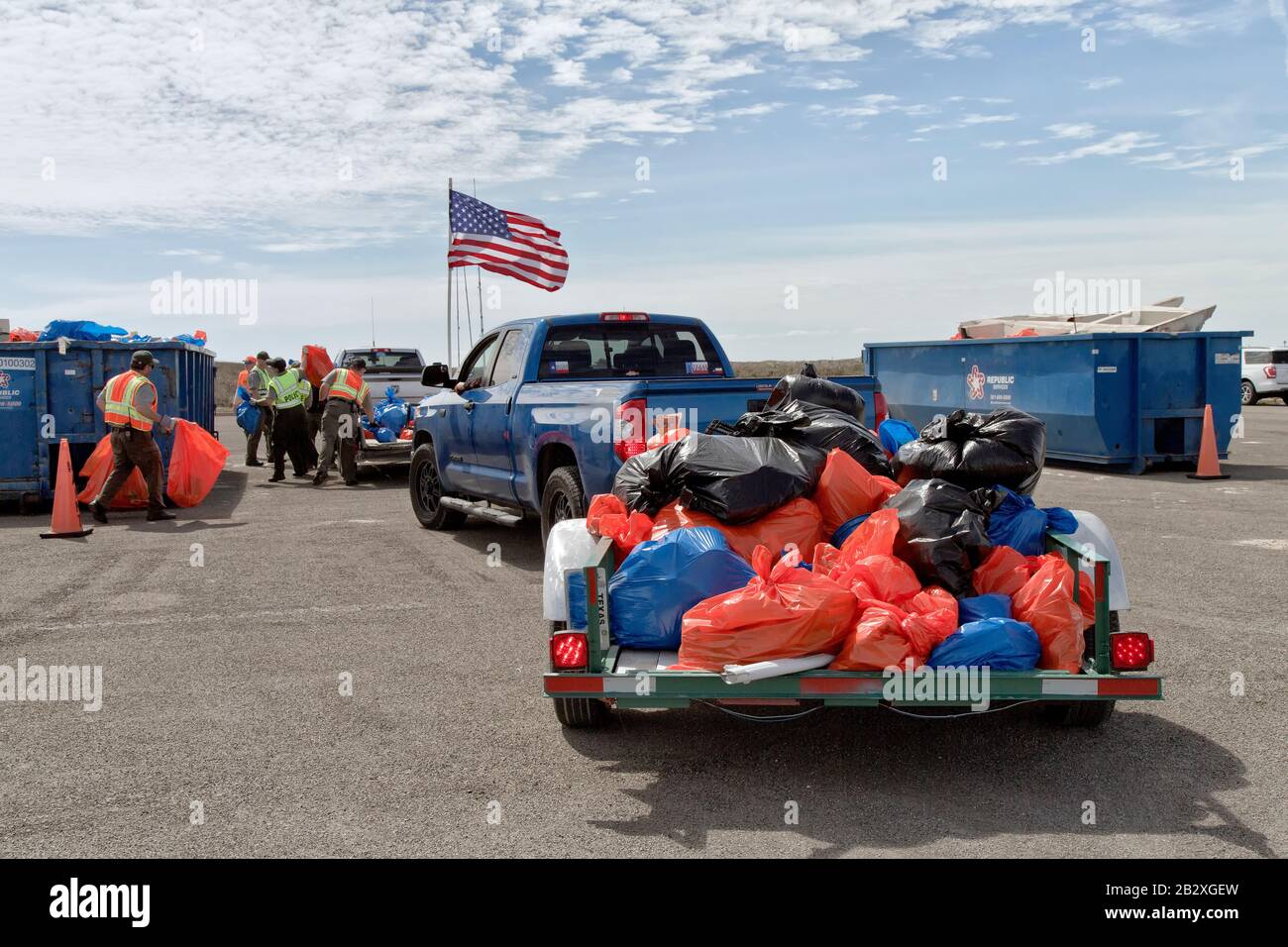 Trailers loaded with marine debris & shoreline trash collected by volunteers, park personel & volunteers depositing into trash bins. American Flag. Stock Photo