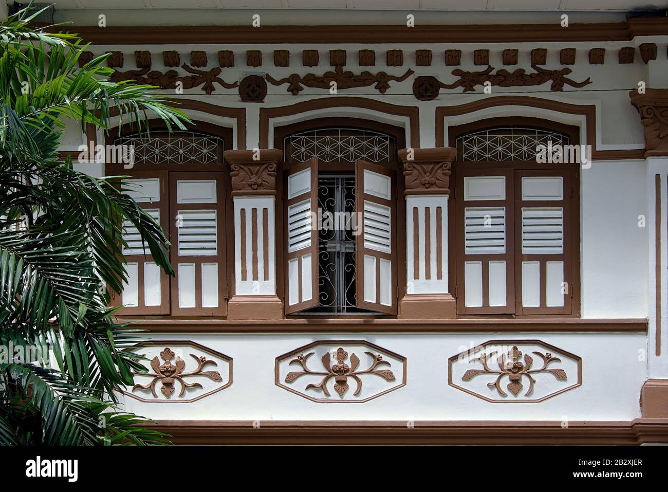 Singapore shophouse with brown and white wooden shutters and ornate stonework in historic Geylang in exterior front view Stock Photo