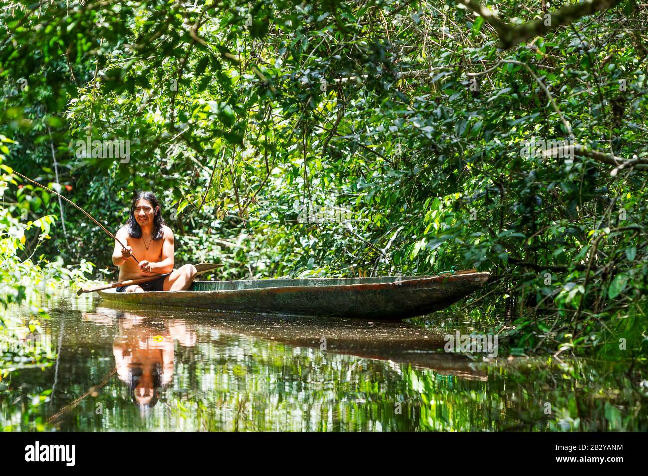Aboriginal Grown Man On Ordinary Wooden Boat Shredded From A Single Tree Cruising Murky Waters Of Ecuadorian Amazonian Primary Rain Forest Stock Photo
