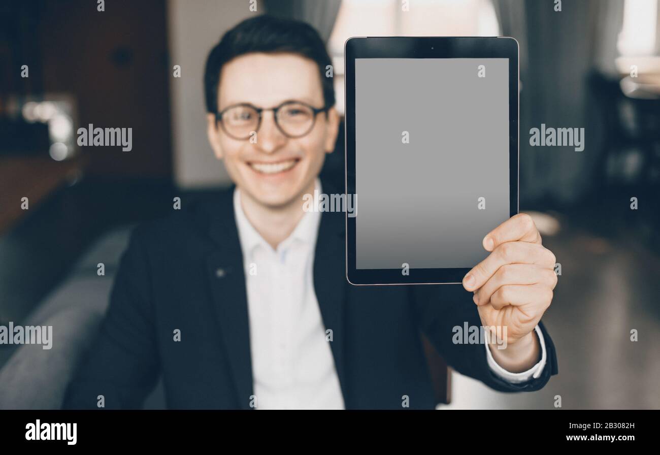 Smiling caucasian businessman dressed in a suit is showing a tablet ...