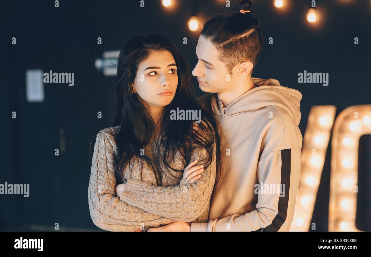 Caucasian man with special haircut is embracing his girlfriend while she is sadly looking at him Stock Photo