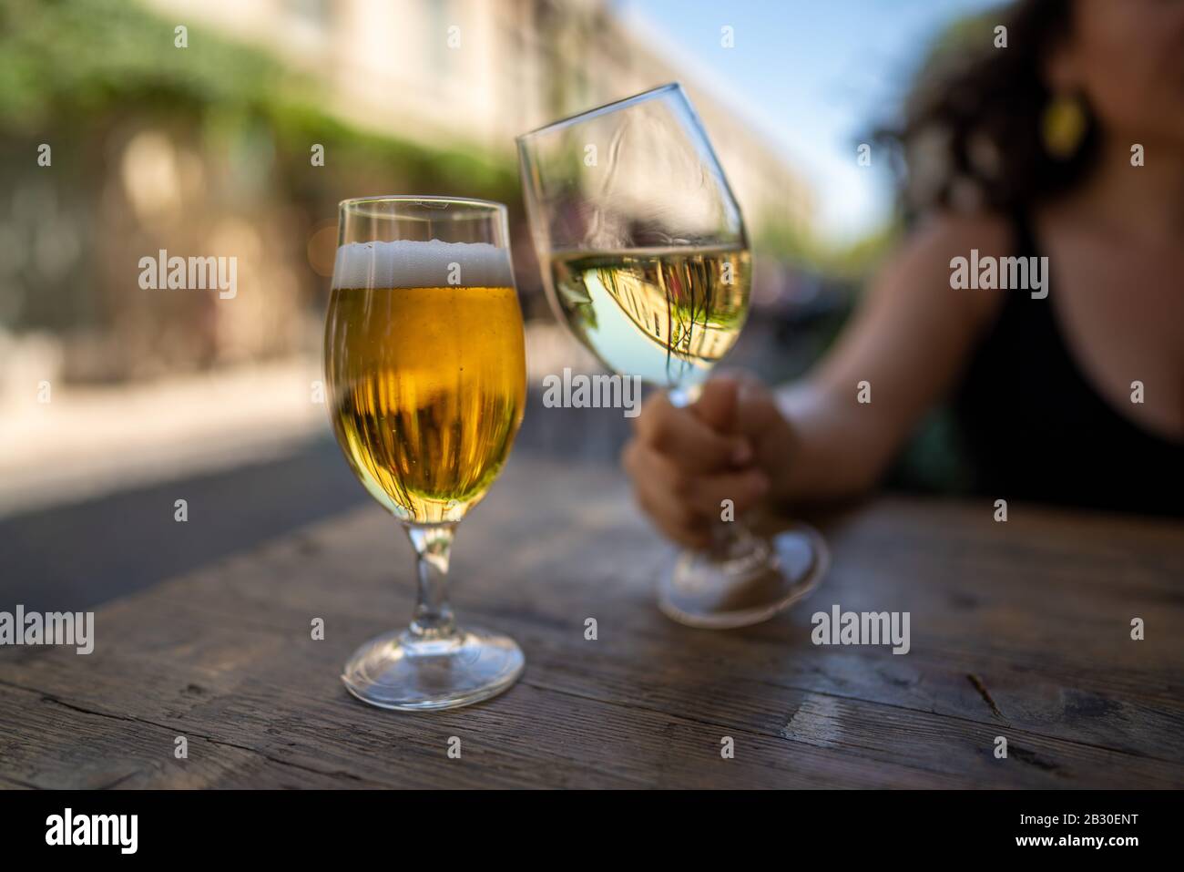 Women holding wine glass next to filled beer glass at outdoor table Stock Photo