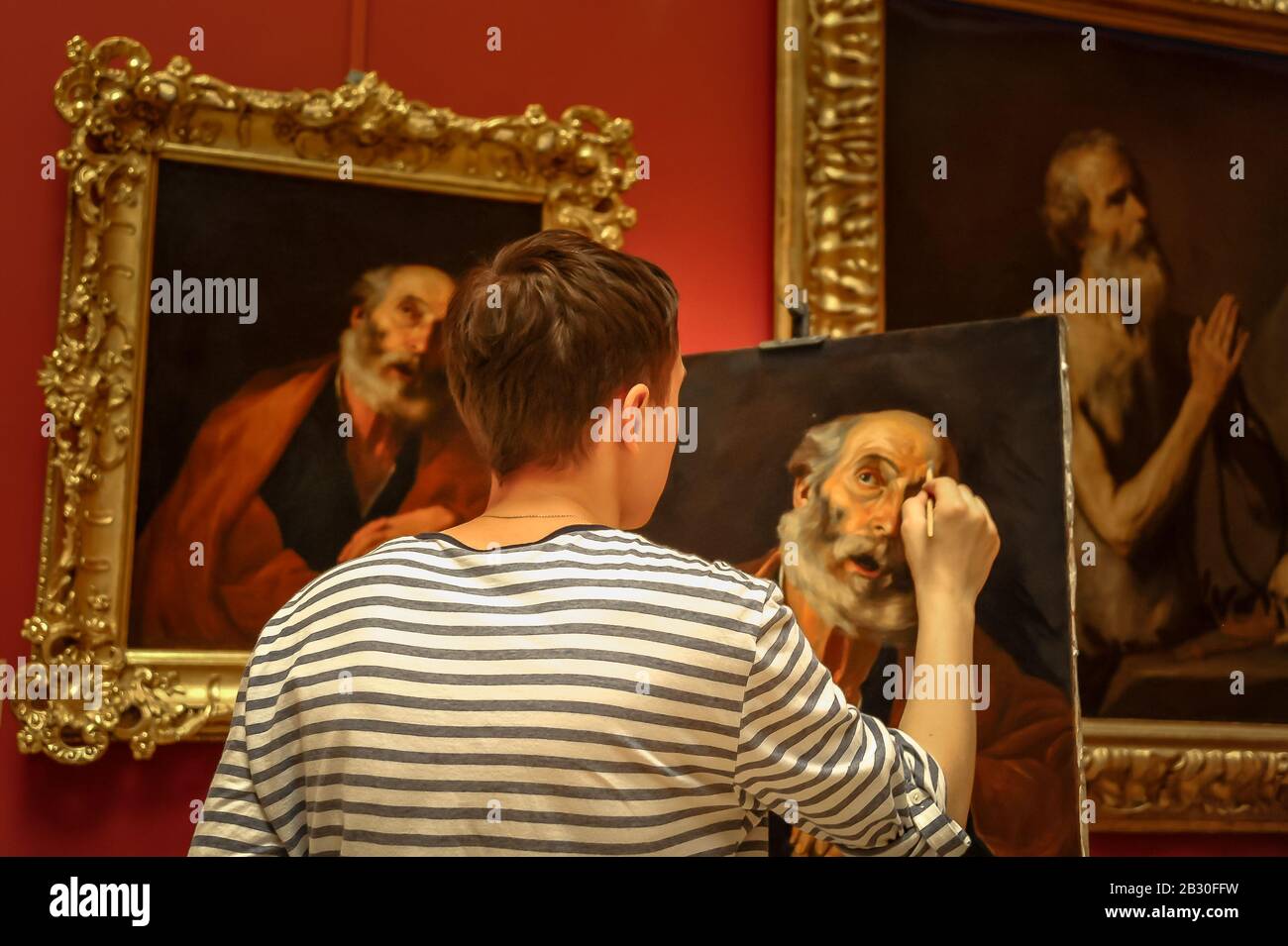 Russia, St Petersburg - July 13, 2015: A young male student with back to camera makes a copy of old oil painting at The Hermitage Museum Stock Photo