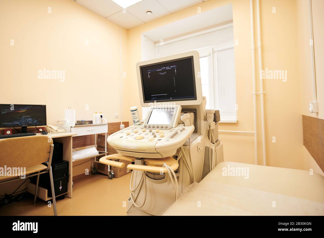 Modern ultrasound machine placed at examination couch in procedure room