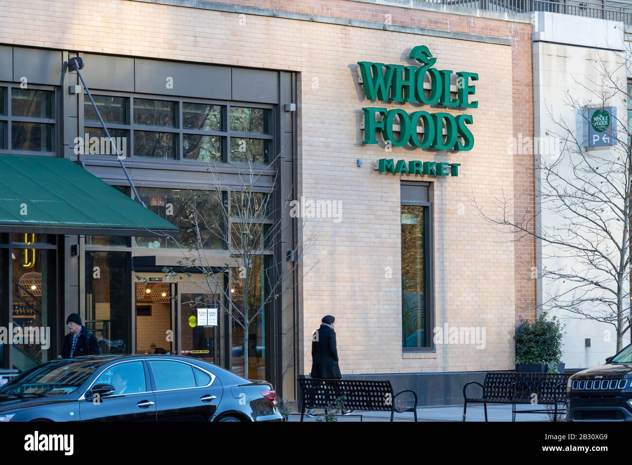 Whole Foods Market sign at an entrance to the popular supermarket chain as a customer walks out. Stock Photo