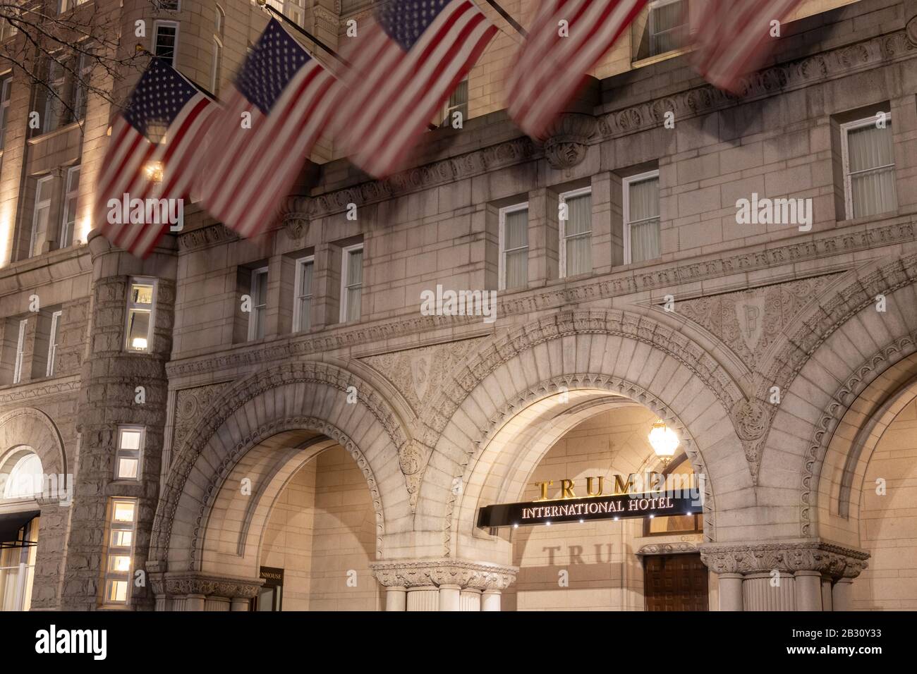 Trump International Hotel sign in-focus at the main entrance on Pennsylvania Ave in Washington, D.C. with American flags waving above at night. Stock Photo