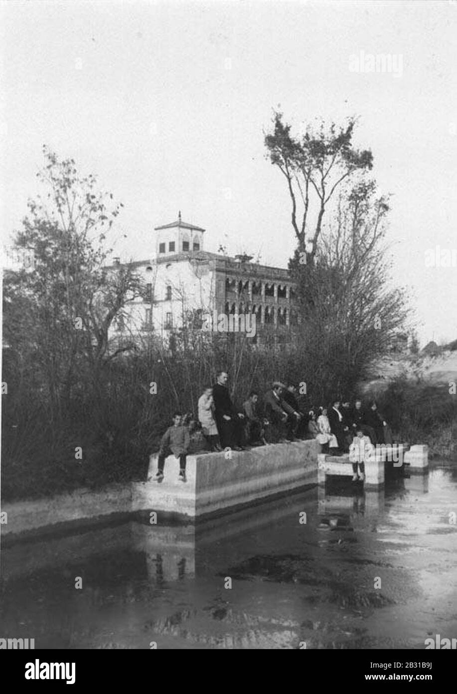 Gent asseguda vora un llac i el Ricart de Malla al fons. Stock Photo