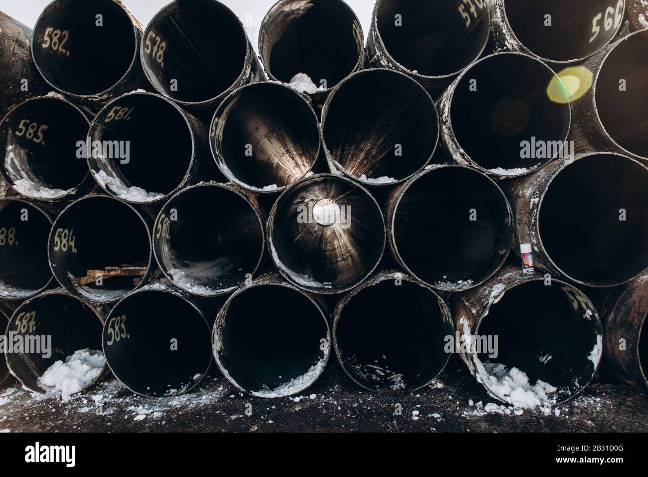 Old used oil pipes. Sunlight passes through the pipes. The tube are stacked in a row. The pipes are signed. Stock Photo