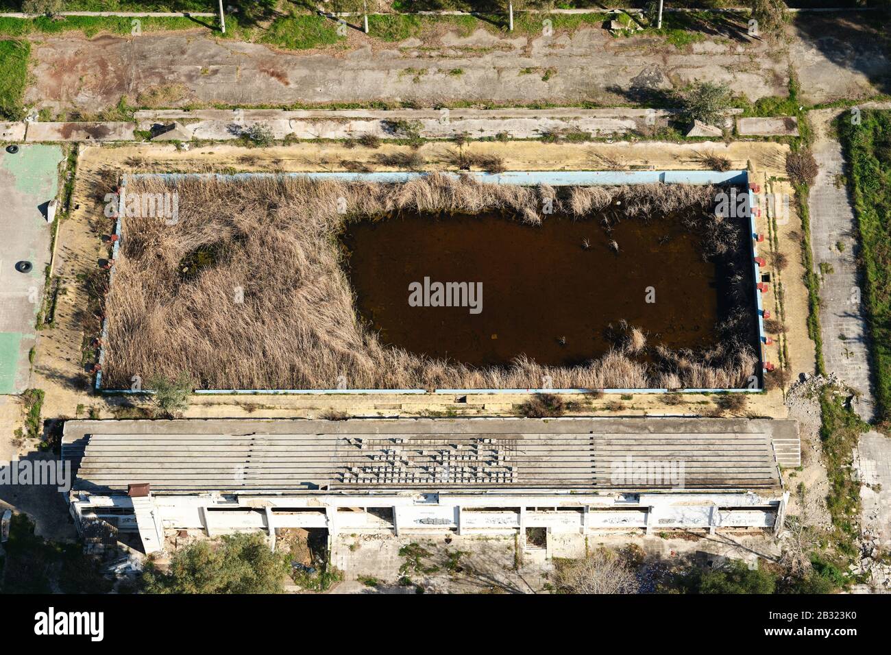 AERIAL VIEW. Abandoned olympic-size swimming pool reclaimed by vegetation. Patras, West Greece, Peloponnese Peninsula, Greece. Stock Photo