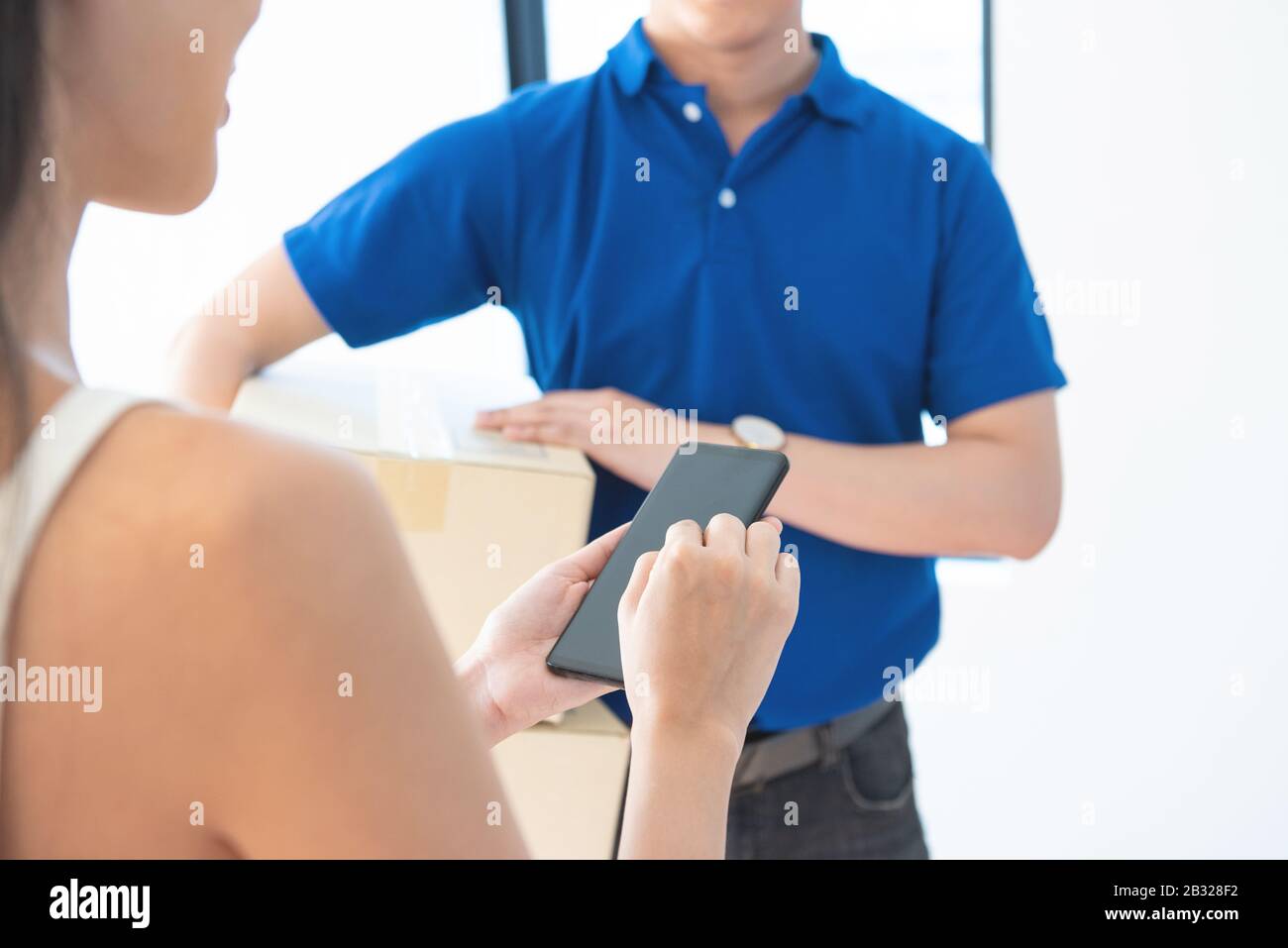 View of young asian woman appending signature in digital smart mobile phone after receiving parcel from courier delivery man at home.AI Technology tra Stock Photo