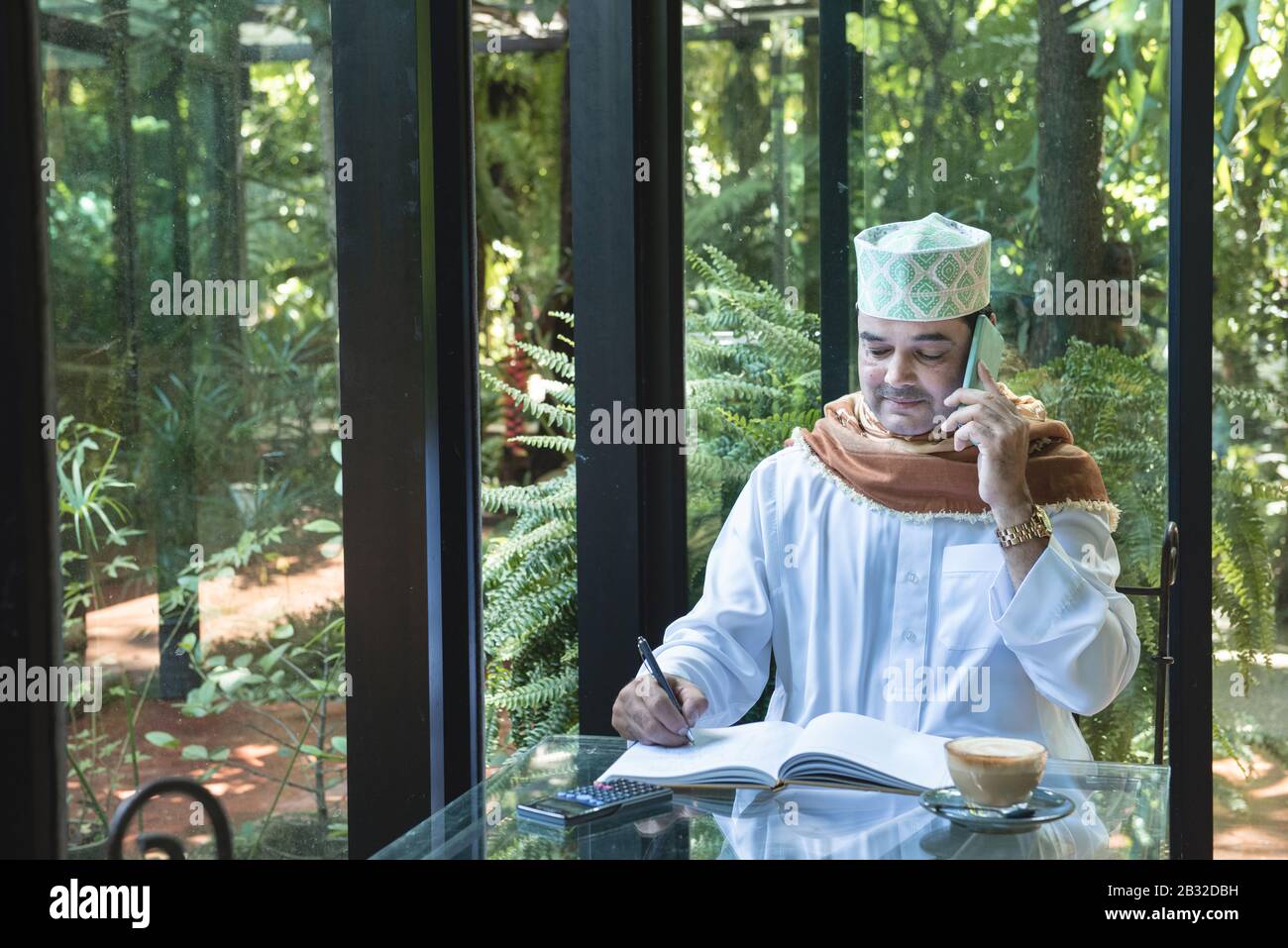 Arab muslim businessman use smartphone communication and write on book in coffee shop ,freelance no working space lifestyle. Stock Photo
