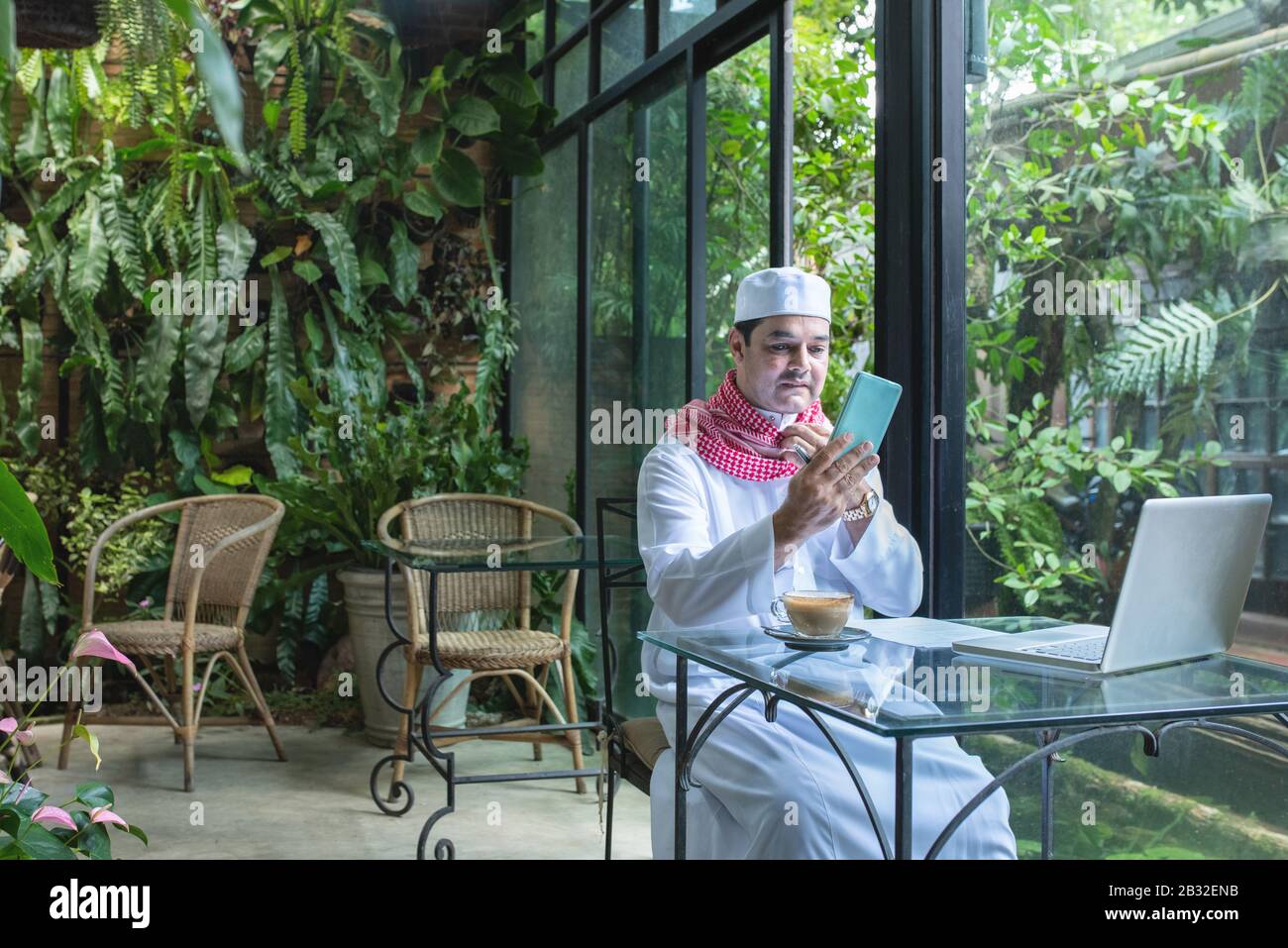 Arab muslim businessmen wear white traditional clothing in hand use smart phone and open laptop on coffee glass table Stock Photo