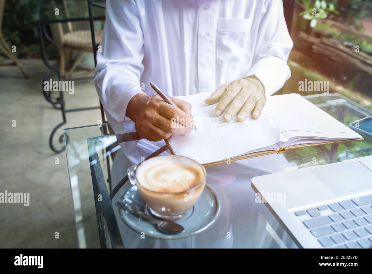 Young handsome businessman arab muslims in coffee shop wearing hijab dressed  write on book file with laptop on table.focus on hand. Stock Photo
