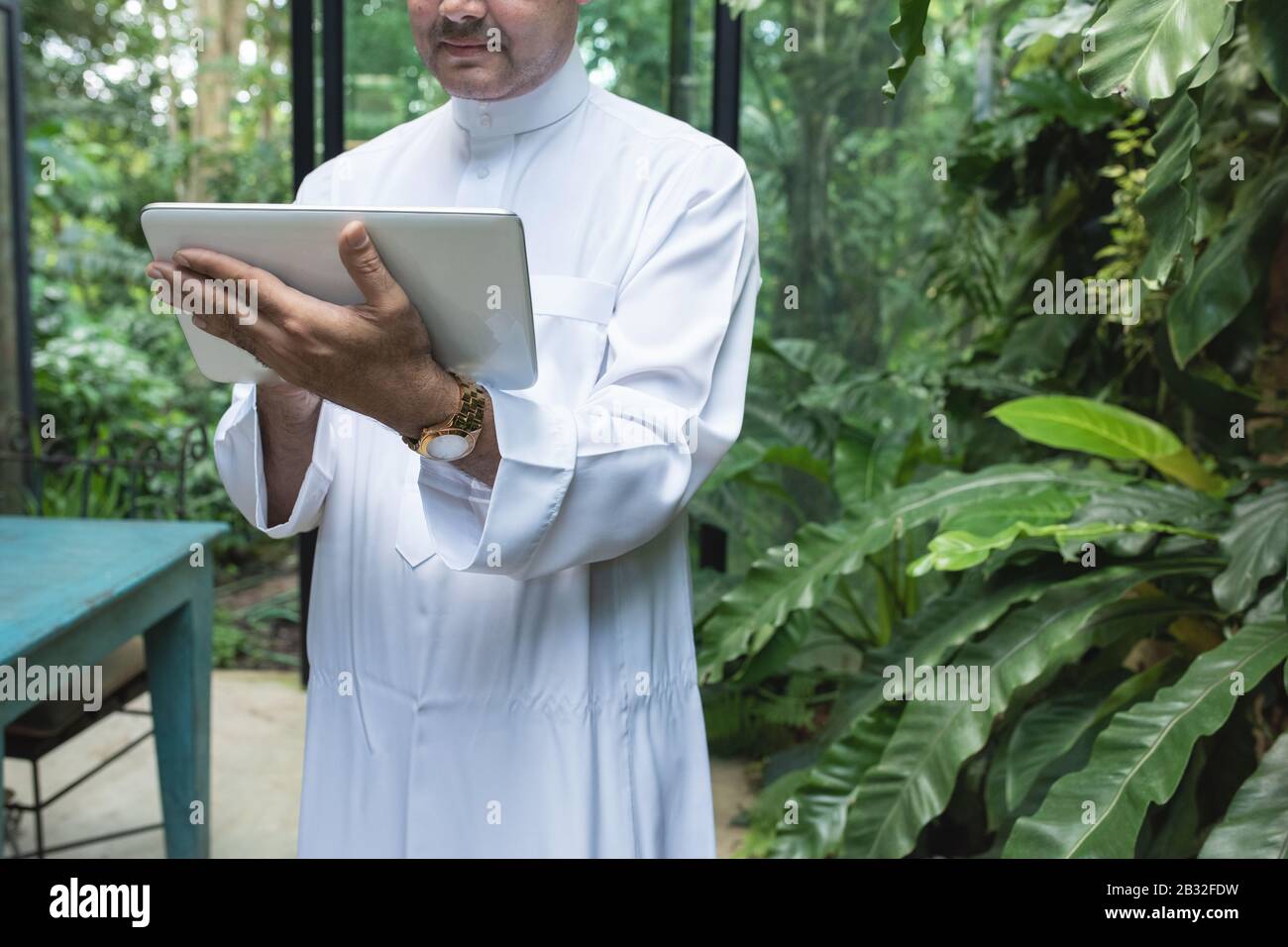 Saudi business asian man using tablet,standing in green cafe wear muslim dress ,freelance business concept. Stock Photo