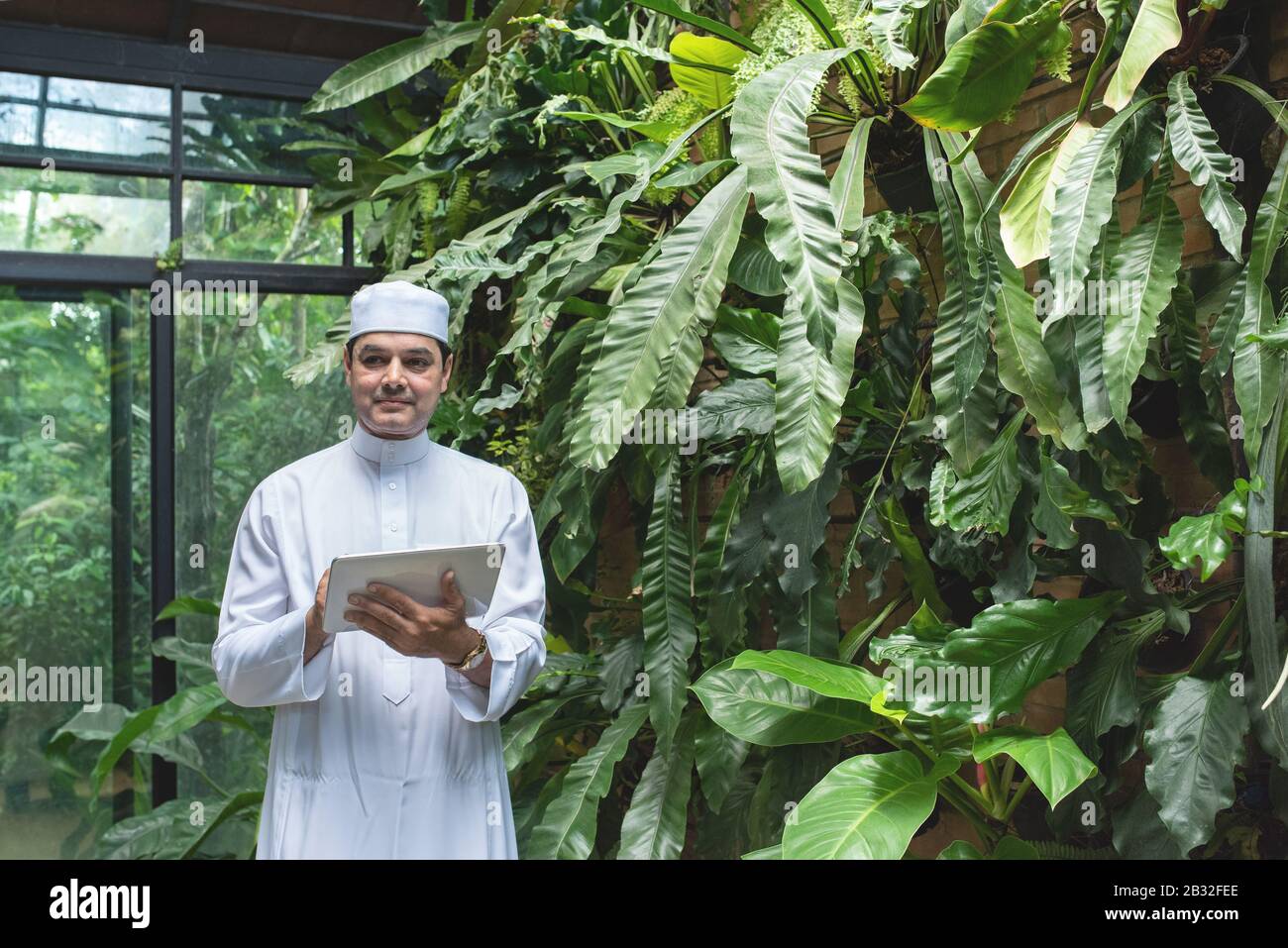 Arab business asian man using tablet,standing in green cafe wear muslim dress ,freelance business concept. Stock Photo