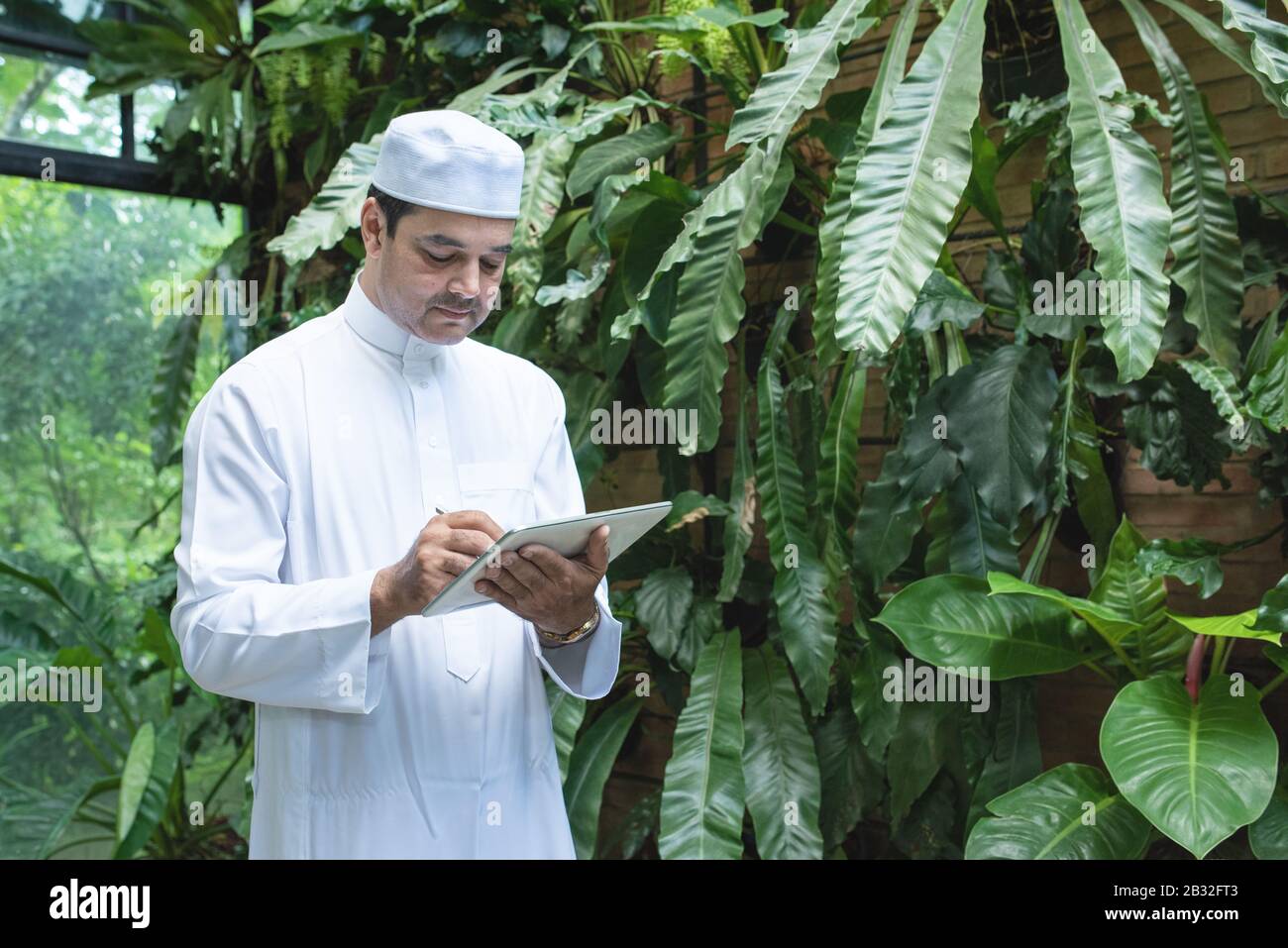 Pakistani business asian man using tablet,standing in green cafe wear muslim dress ,freelance business concept. Stock Photo