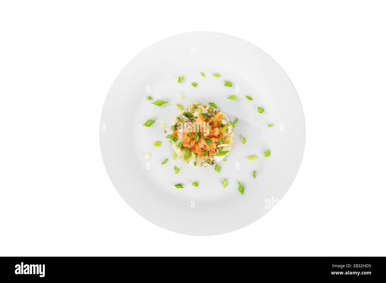 Russian salad with peas, red fish, chum salmon, eggs, cucumbers, carrots, potatoes, decorate green onion on plate, view from above, white isolated bac Stock Photo