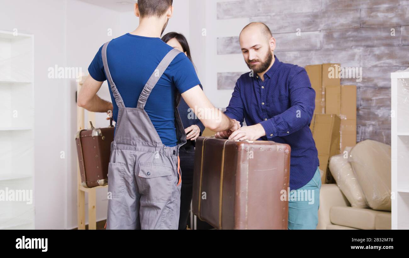 Man from delivery service arriving with suitcases of young couple in their new real estate