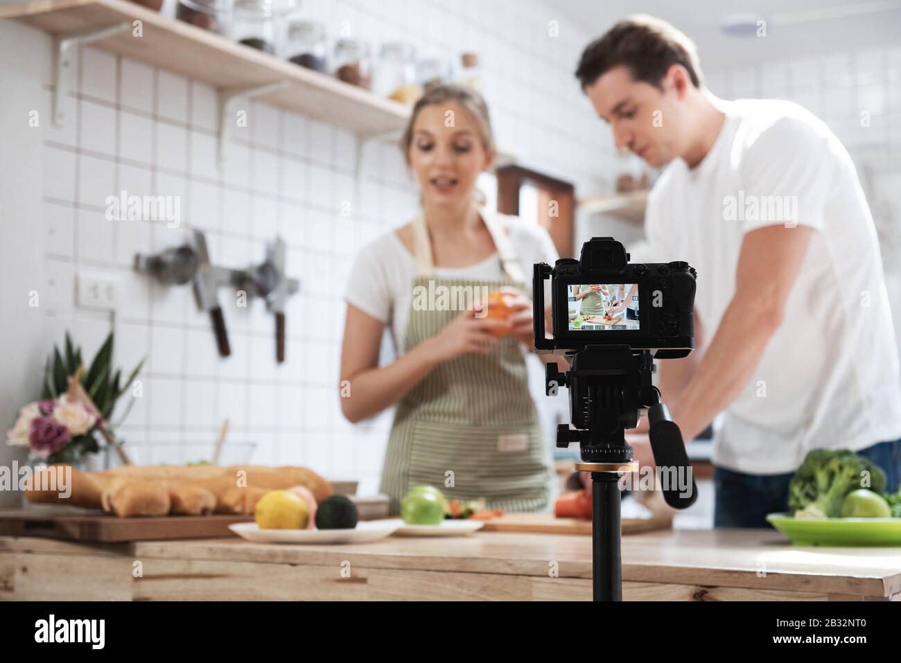 Professional digital mirrorless camera  recording video blog of happy caucasian couple cooking in the kitchen room. Stock Photo