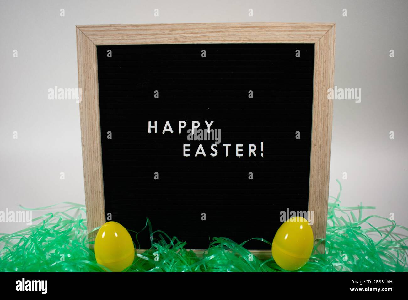A Black Happy Easter Sign With White Letters, Easter Grass, and Easter Eggs Stock Photo