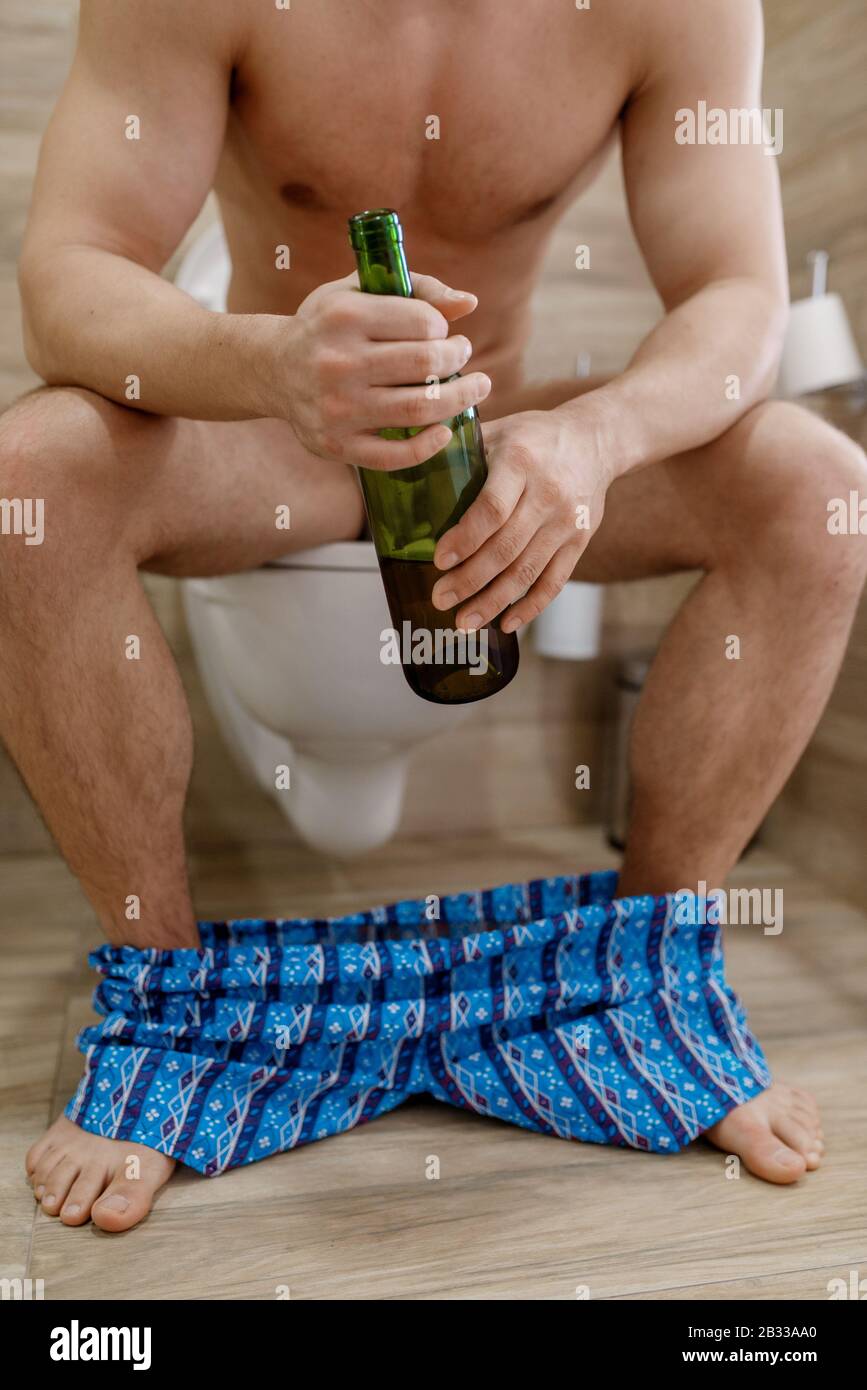 Hangover man with bottle of wine sitting on toilet Stock Photo