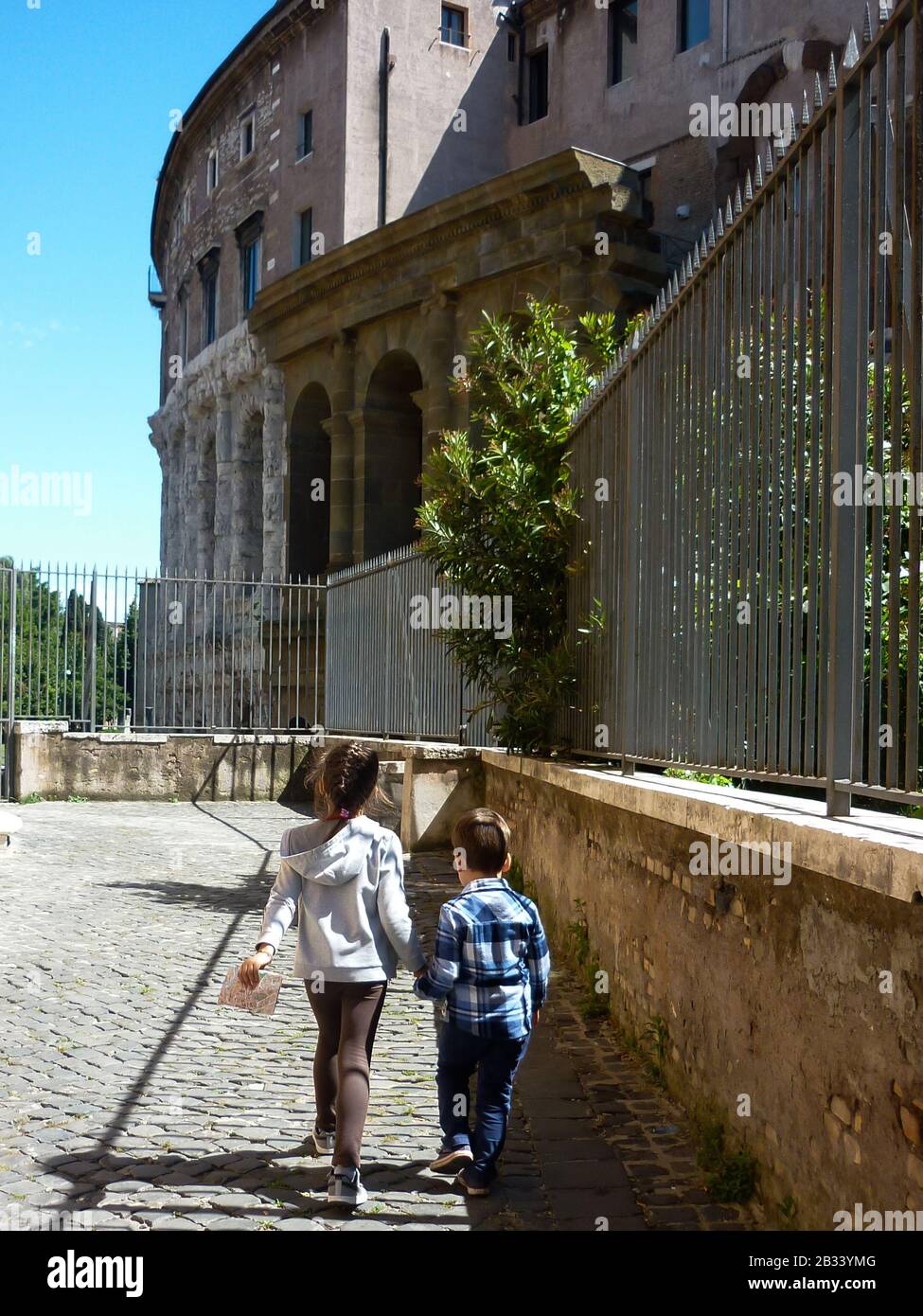 Rear view of children walking hand in hand through the historic center of Rome. The little girl holds a travel map in her hand and guides her brother. Stock Photo