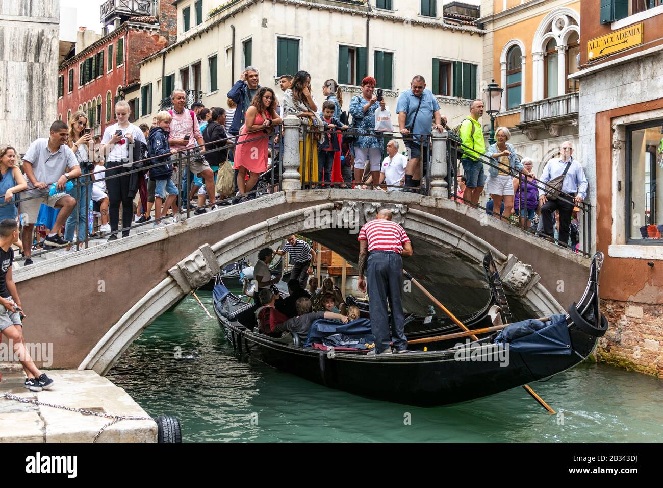 Mass tourism. Crowded bridge over canal, as many tourists watch and photograph the gondola's going by. Venice, Italy Stock Photo