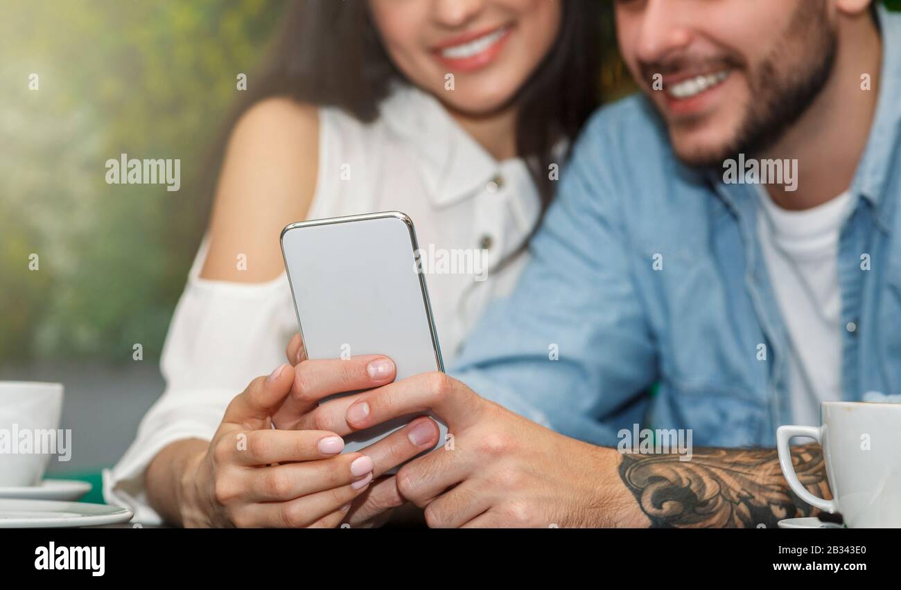 Unrecognizable Couple Using Smartphone Sitting In Cafeteria, Cropped Stock Photo