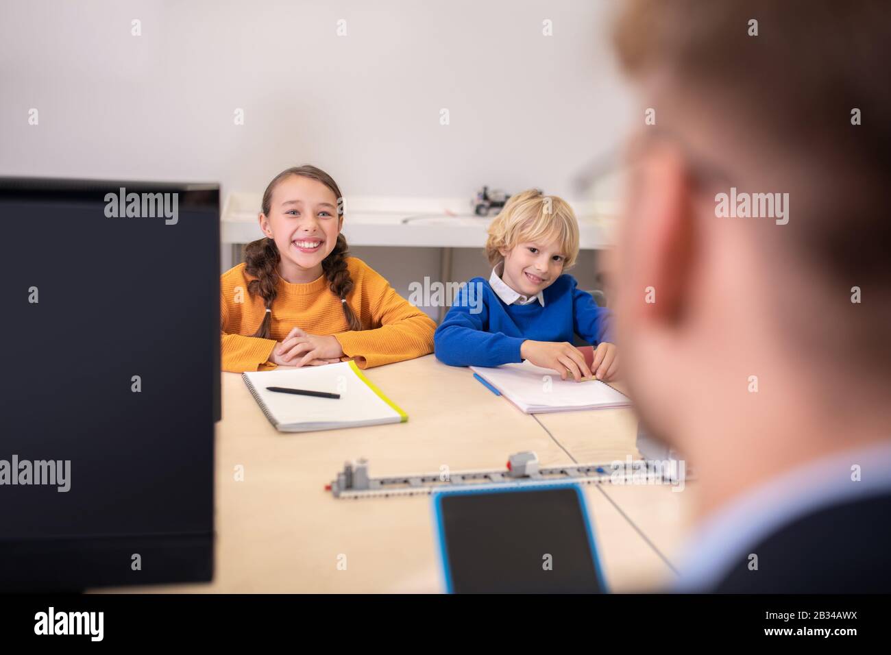 Pupils sitting at the desk opposite teacher, smiling Stock Photo - Alamy