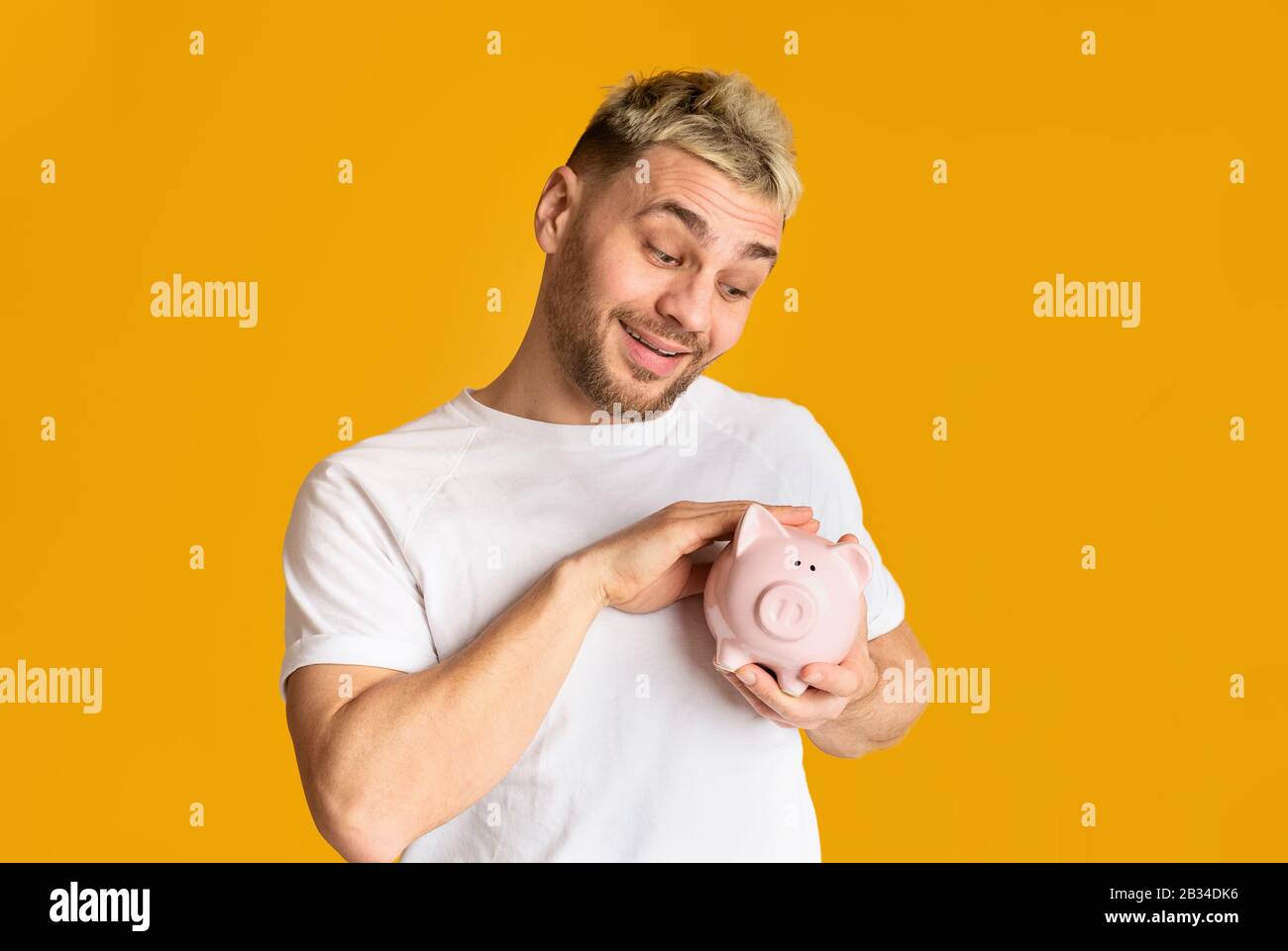 Saving concept. Ridiculous guy stroking piggy bank Stock Photo