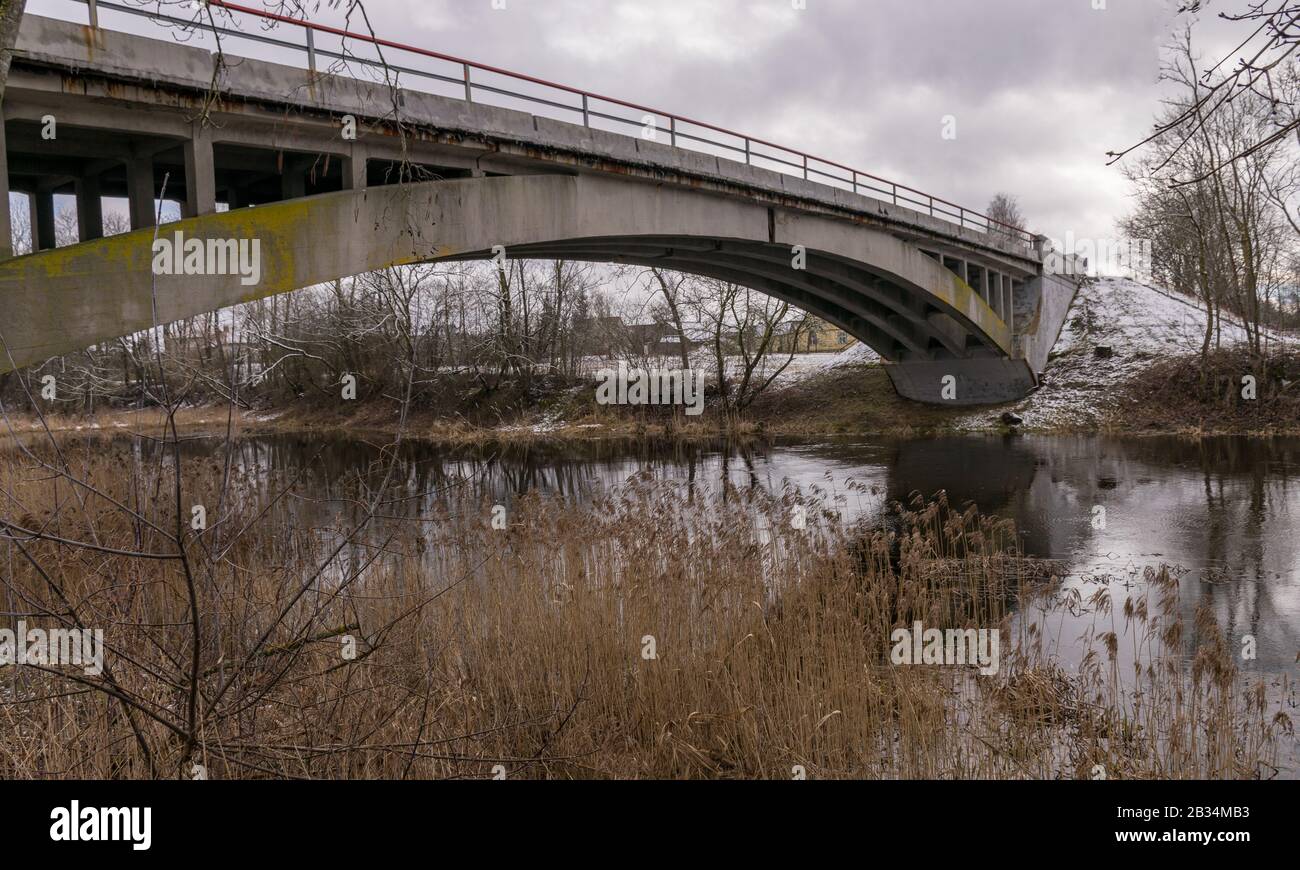 concrete arched bridge over a small and wild river, overgrown with ...