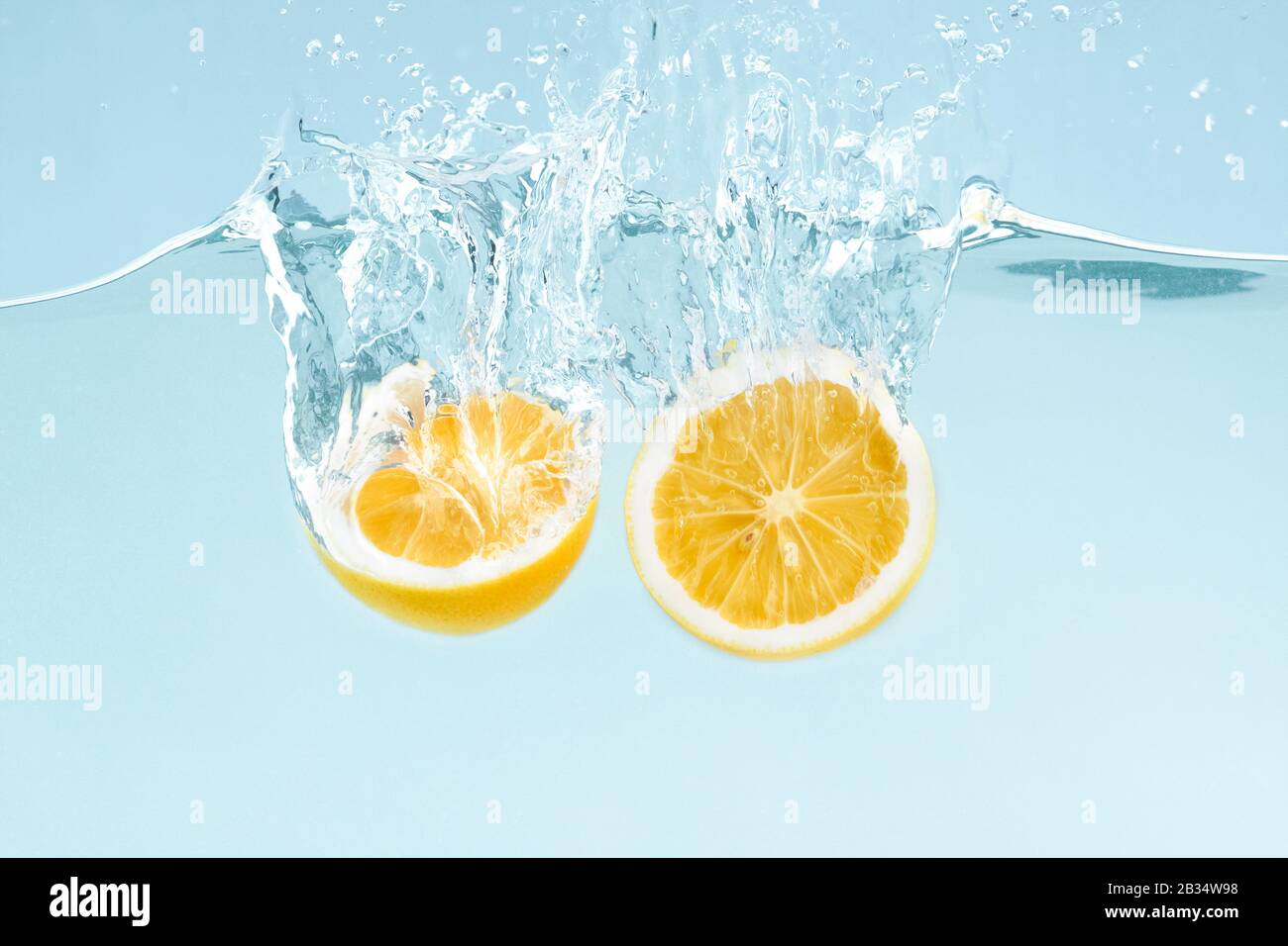 Citrus splash. Lemon halves splattering into clear water on blue background Stock Photo
