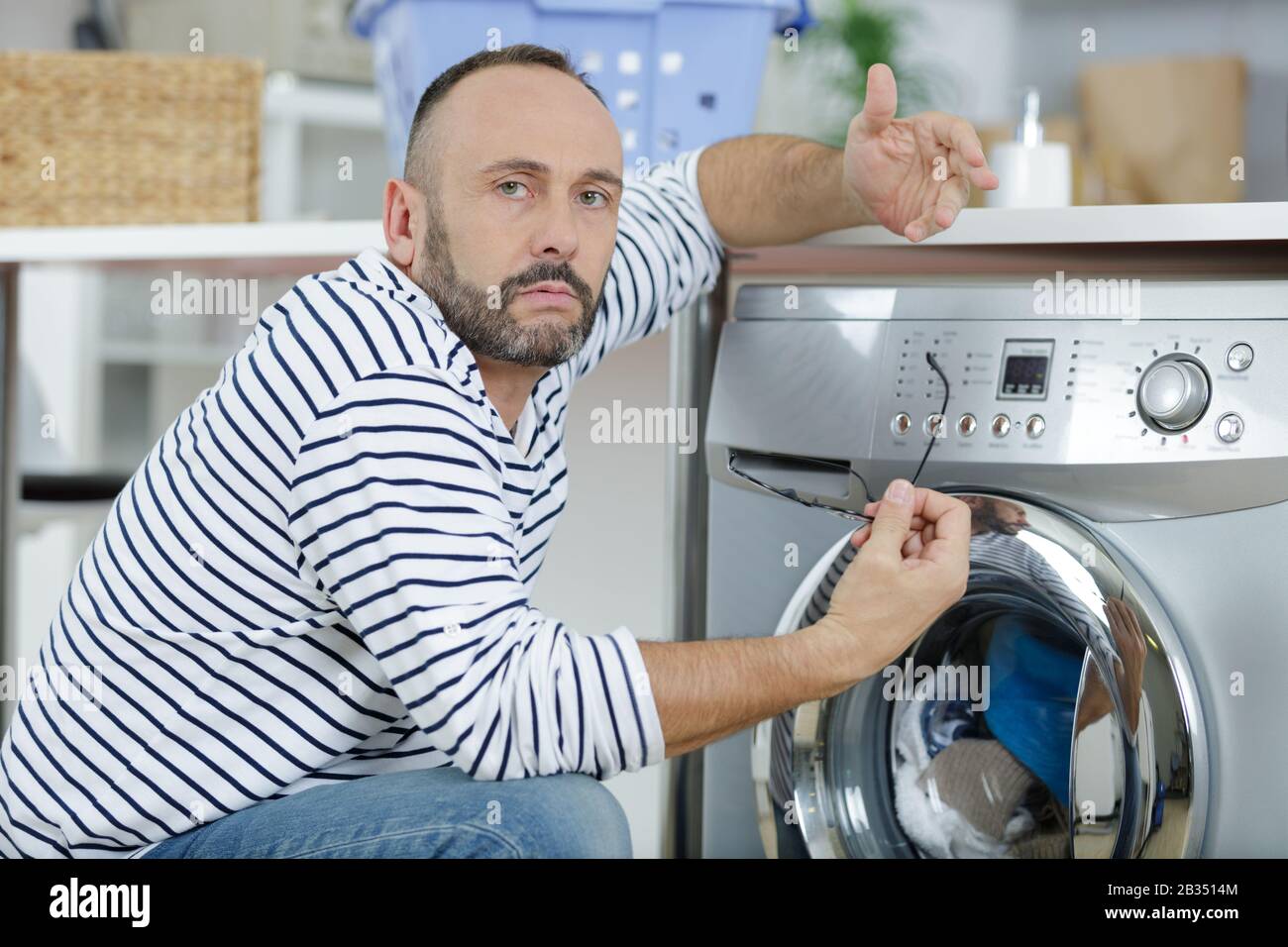 man making gesture of incomprehension towards broken washing machine Stock Photo