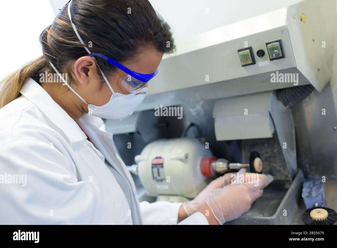 female worker shaping prosthetic teeth on grinding machine Stock Photo