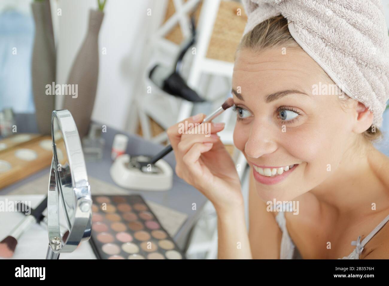 woman wearing towel on head applying make-up eyelashes Stock Photo