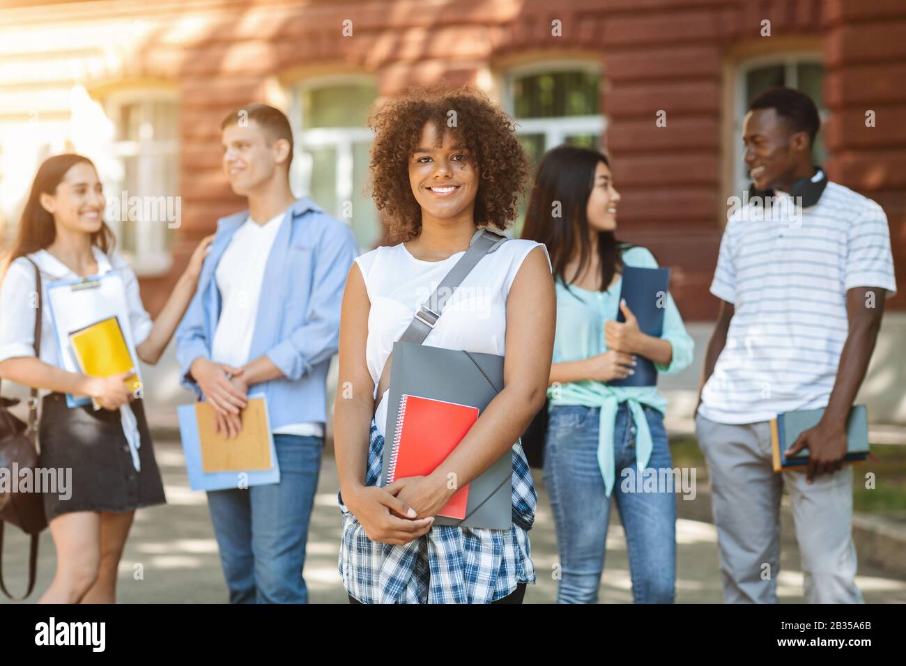 Beautiful african student girl posing outdoors with university friends on background Stock Photo