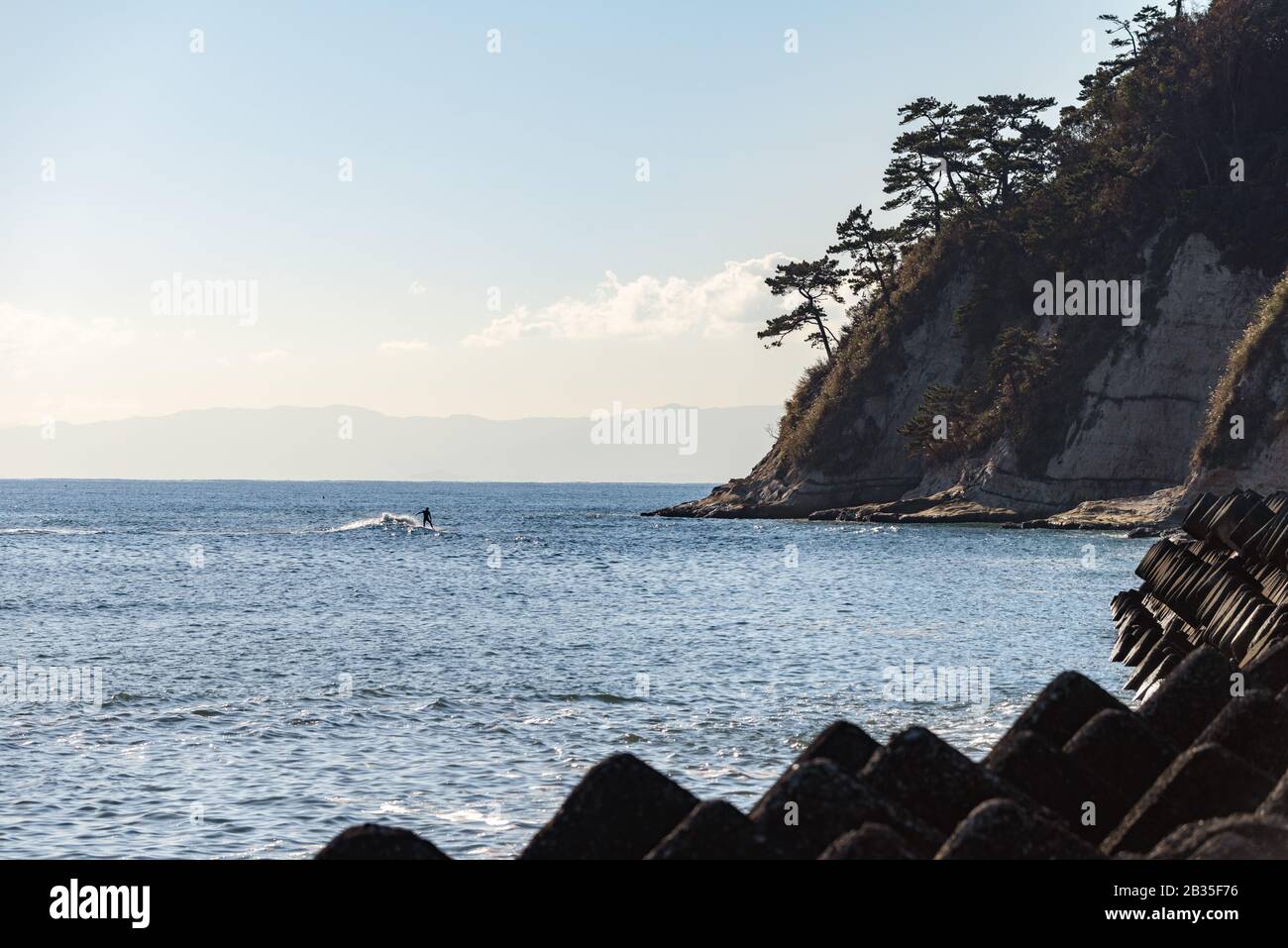 A surfer rides a wave towards Cape Imamuragasaki, Sagami Bay, close to Enoshima Island, setting of the Tokyo 2020 Summer Olympics sailing events Stock Photo