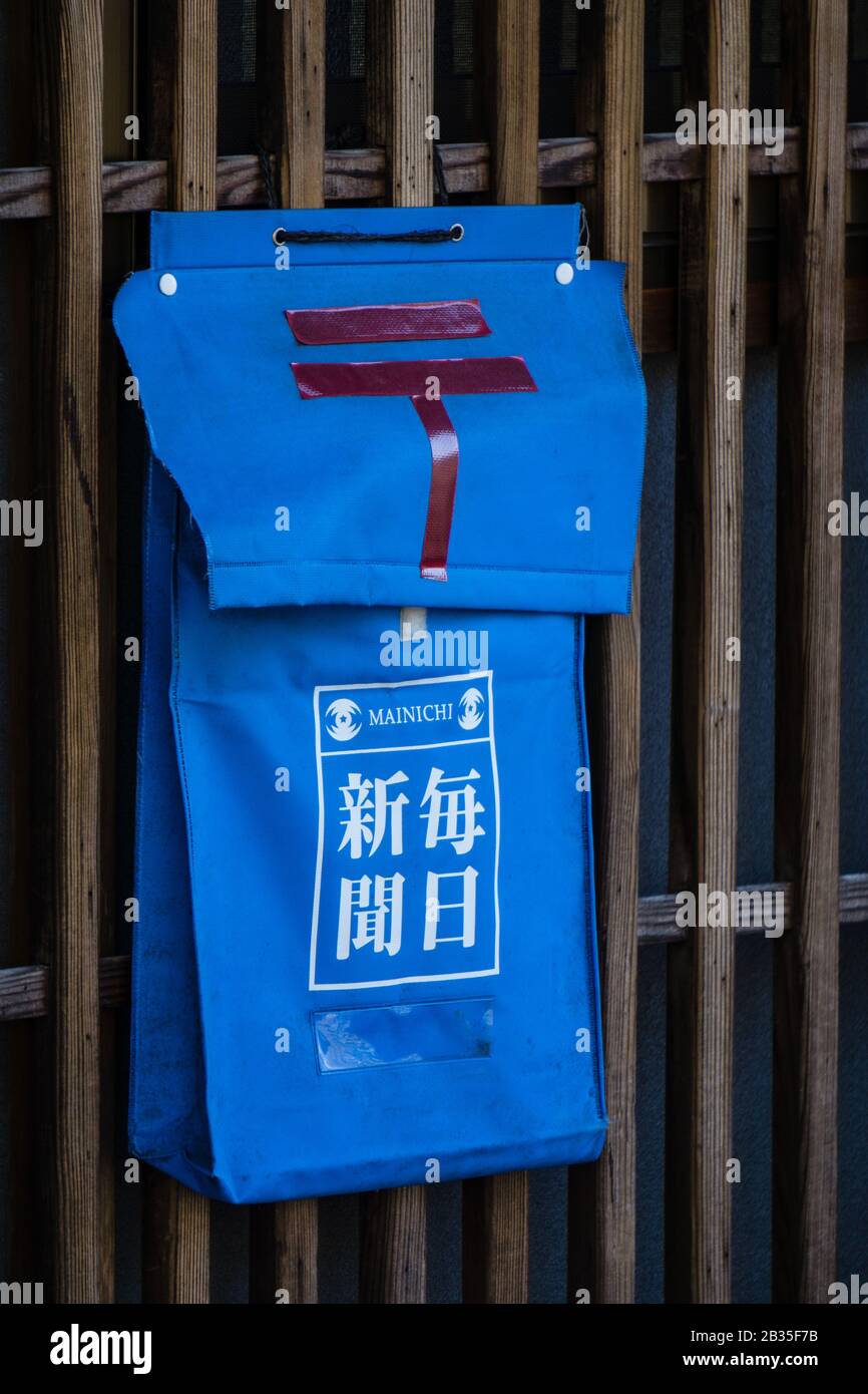 A newspaper and post box on a wooden fence in Nara, Japan. The red symbol is that of the Japanese Post Office. The Kanji reads Mainichi Shimbun. Stock Photo