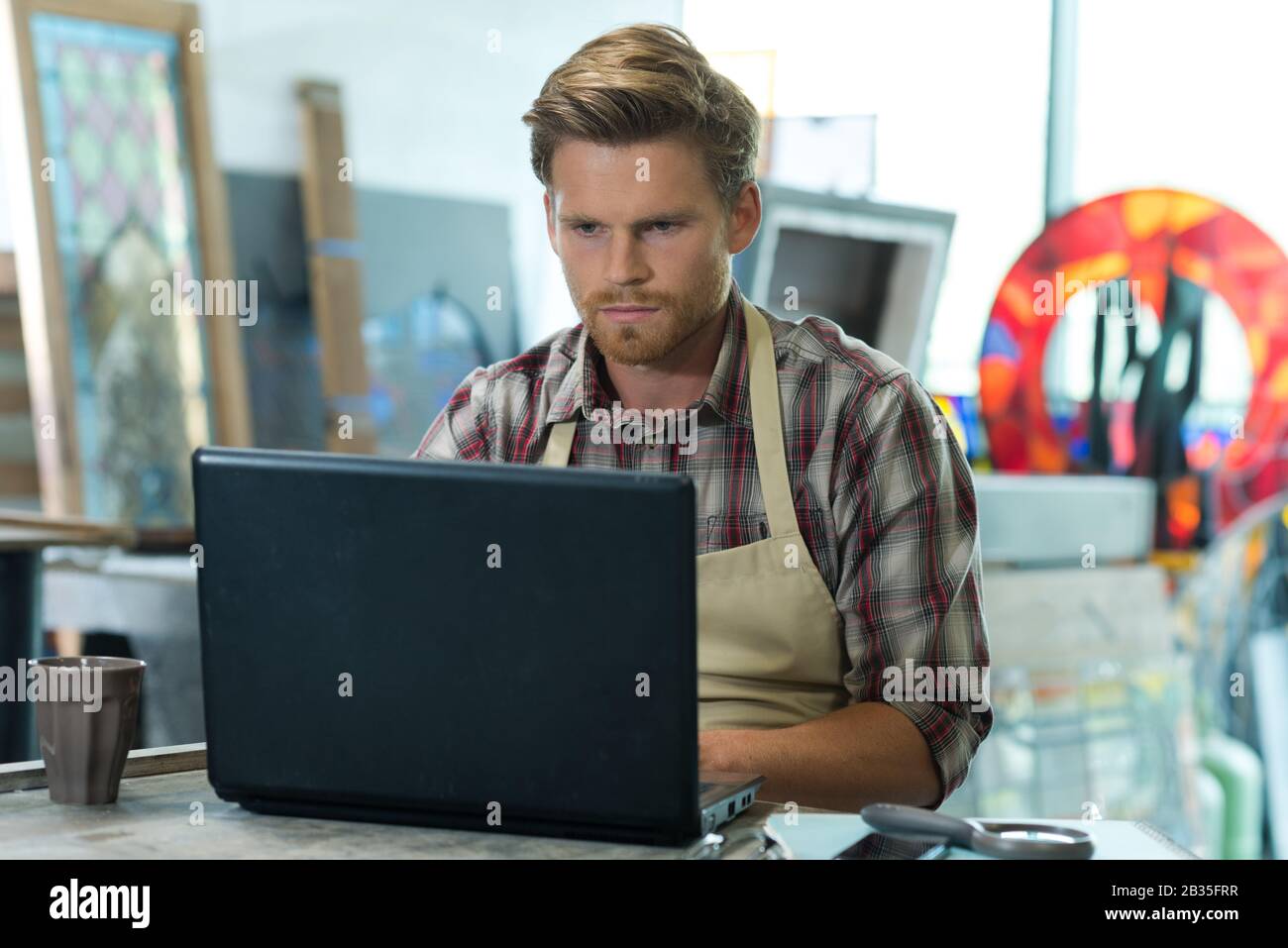 young bearded carpenter using laptop in workshop Stock Photo