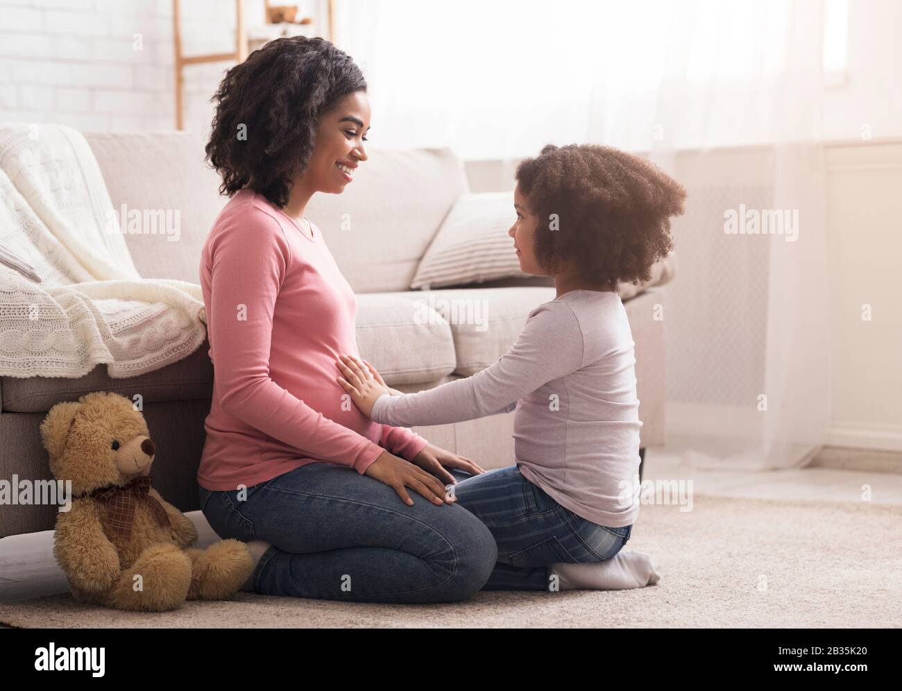 Little daughter touching pregnant mom's belly while playing together at home Stock Photo