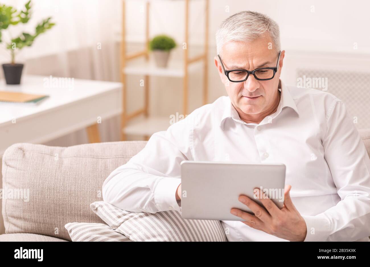 Senior man using digital tablet sitting on sofa Stock Photo
