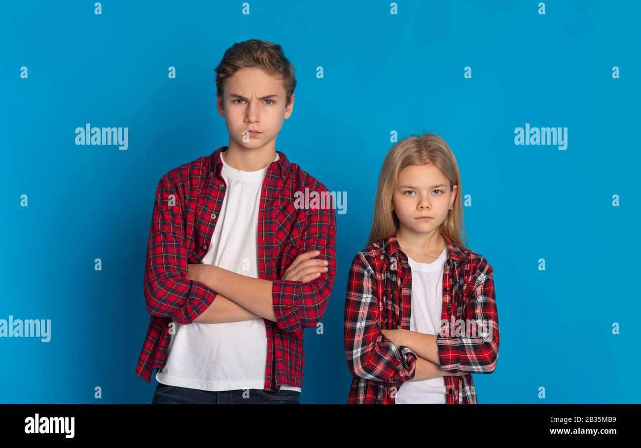 Siblings Conflicts. Frowning Little Brother And Sister Standing With Folded Arms Stock Photo