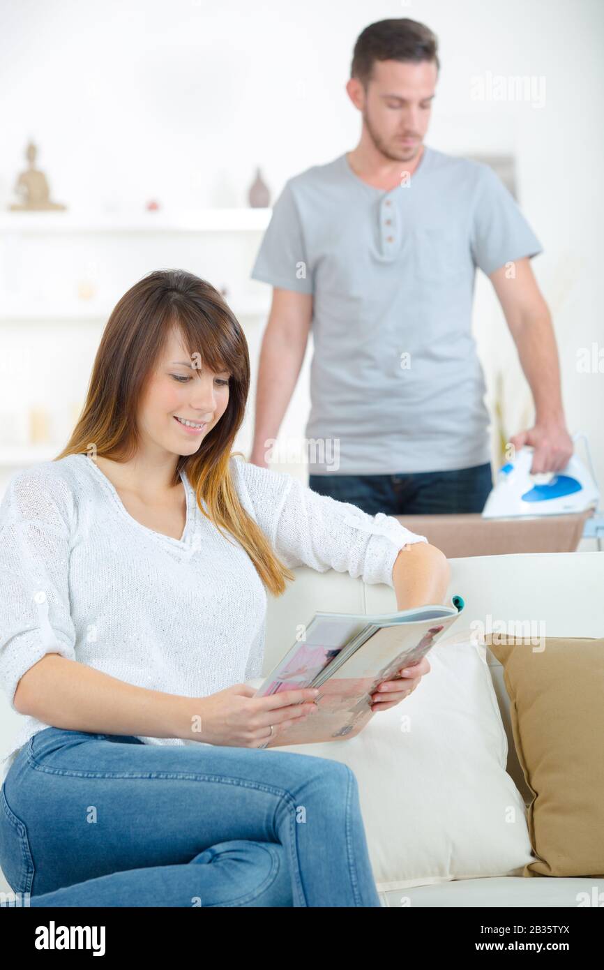 man doing some ironing while girlfriend is reading Stock Photo