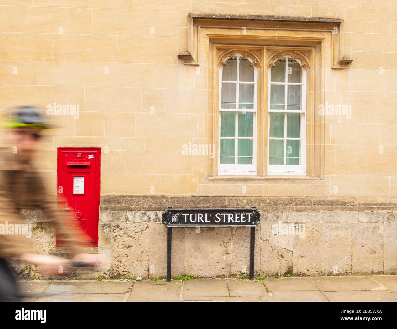 Turl Street in Oxford. Cyclist entering Picture from Right, Motion Blur. Red Post Box, Street sign,Window and Warm Stonework Complete Composition Stock Photo