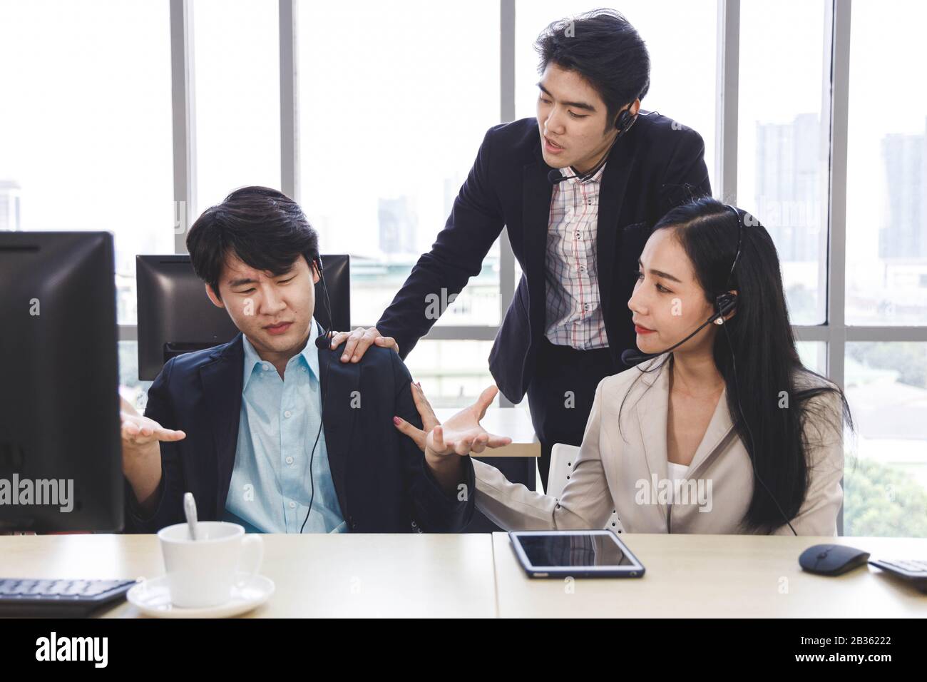 Two Asian call center agents cheer their colleague up who has problem about his work, project or personal life. Stock Photo