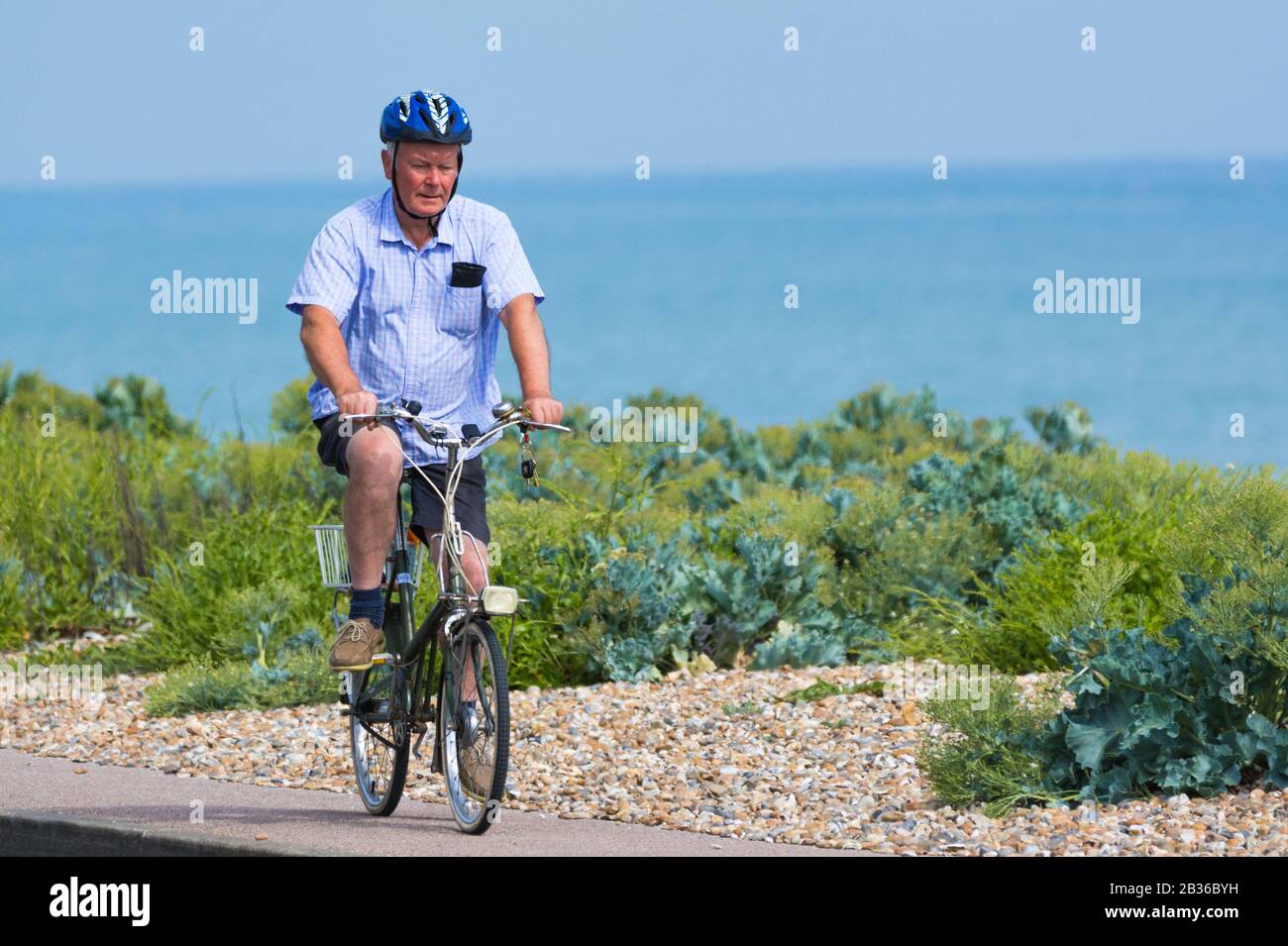 Man wearing cycle helmet riding a bicycle along a seafront pavement by the sea. Male cyclist riding a bike in the UK. Stock Photo