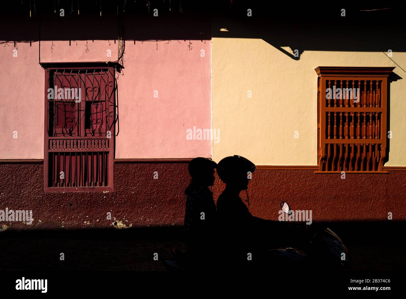 A Colombian couple ride a motorbike in front of a (post)colonial house in Sonsón, a village in the coffee region (Zona cafetera) of Colombia. Stock Photo